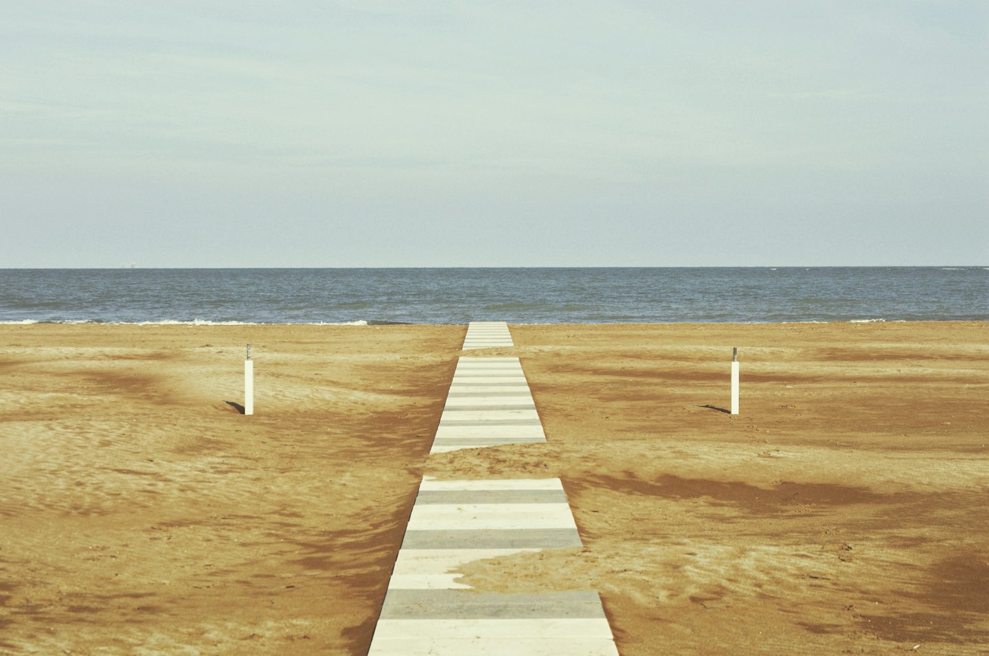 Pasarela de madera que cruza dunas de arena hacia el océano.