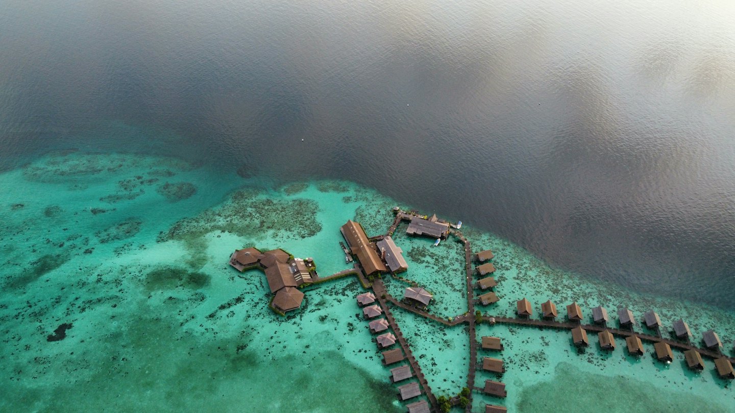 Bungalows de resort tropical conectados por pasarelas de madera sobre agua clara.