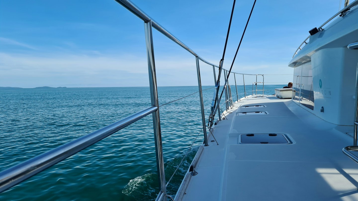 Catamarán blanco navegando en aguas azules tranquilas con tierra a lo lejos.
